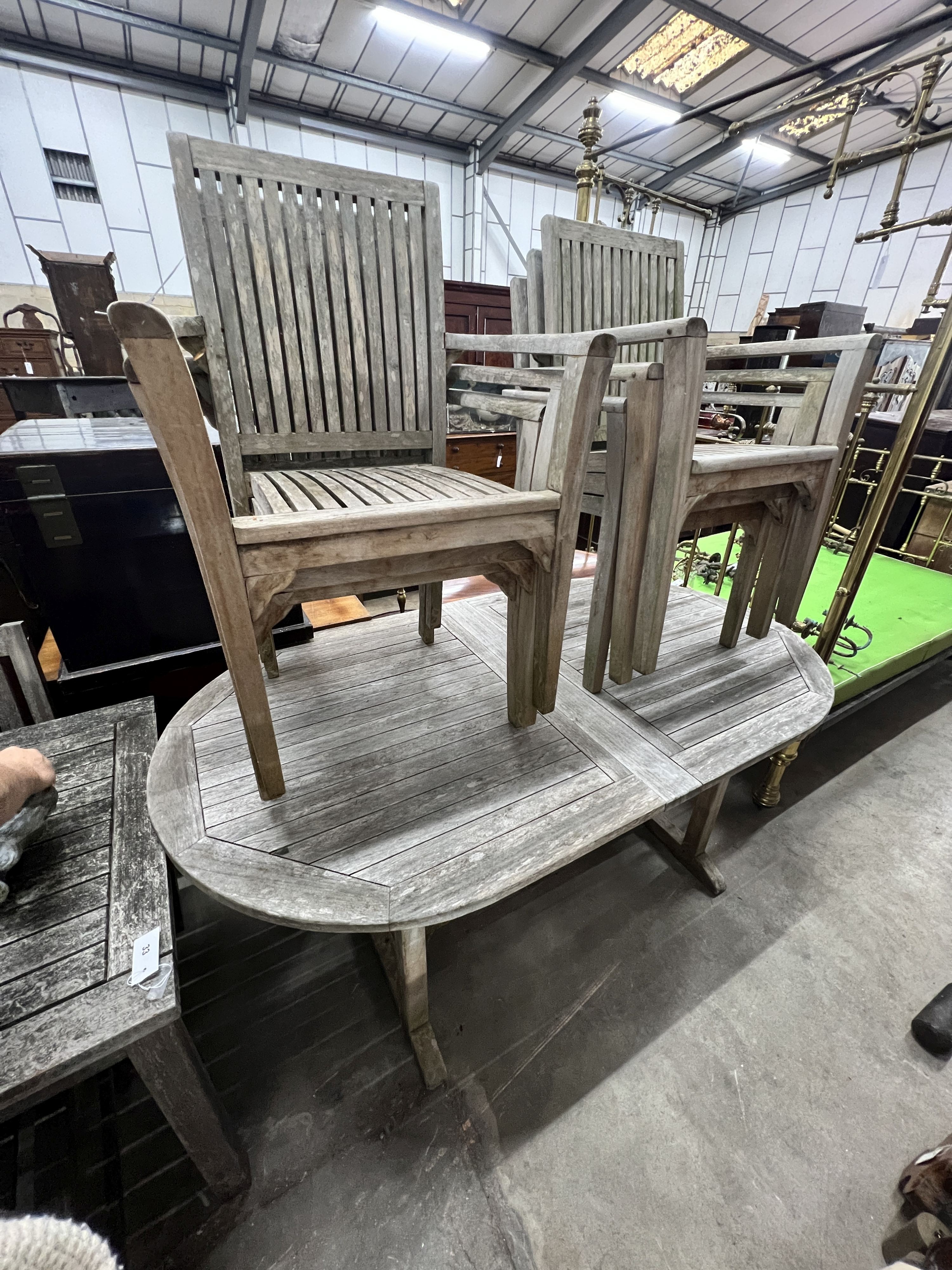 An oval weathered teak extending garden table, width 180cm, depth 100cm, height 76cm and six teak stacking chairs